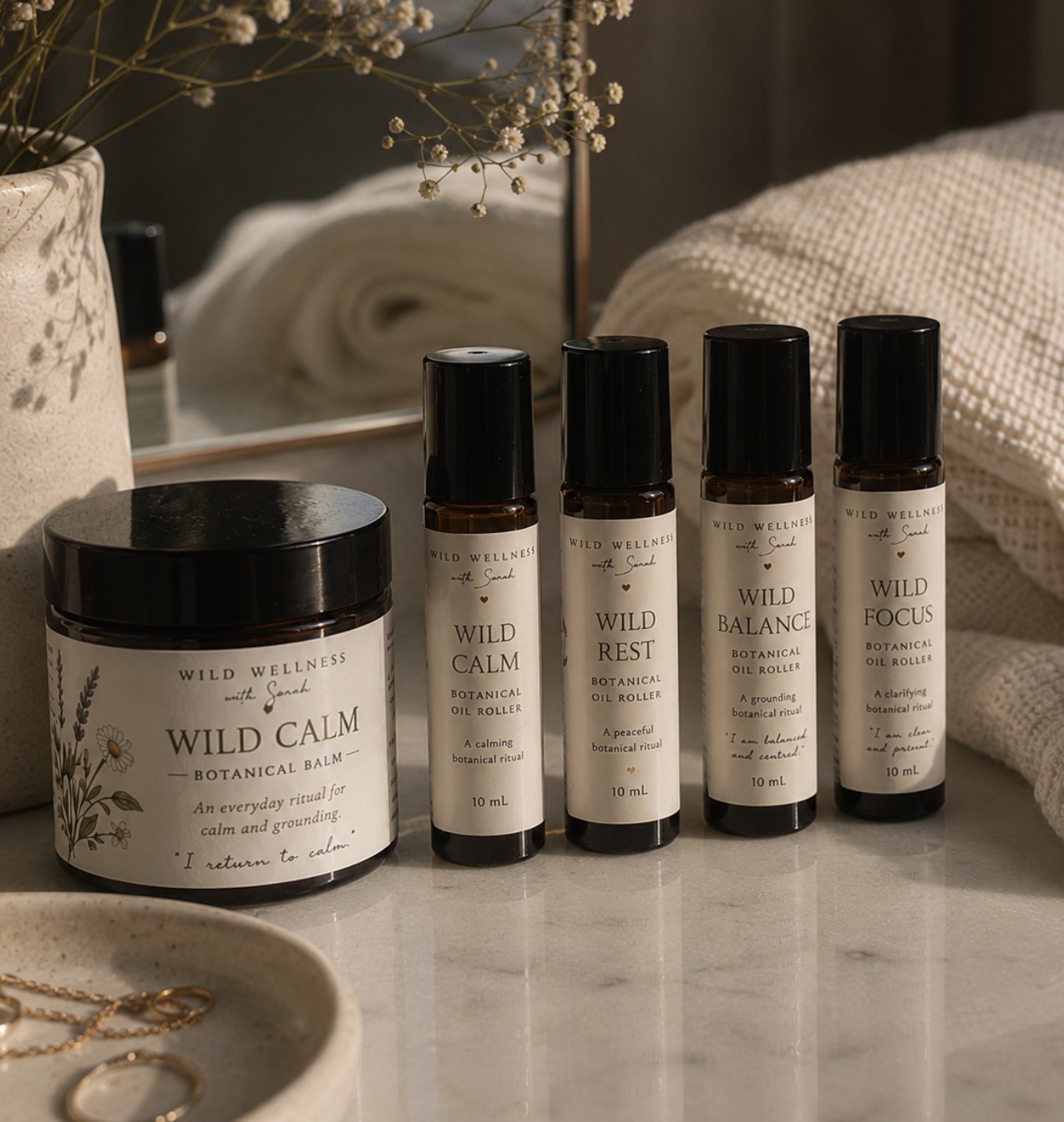 Wild Calm botanical balm with Wild Calm, Wild Rest, Wild Balance and Wild Focus oil rollers styled on stone